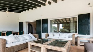 A spacious outdoor seating area with wicker furniture, a glass-top coffee table, and a view of the outdoors. - Big beautiful villa sleeps 10: sea view, beach 5 minutes and everything nearby (Es Mercadal)