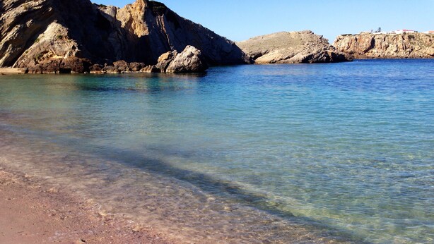 A clear beach with rocky formations in the background. - Big beautiful villa sleeps 10: sea view, beach 5 minutes and everything nearby (Es Mercadal)