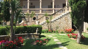 A courtyard with a stone staircase, palm trees, and red flowers.