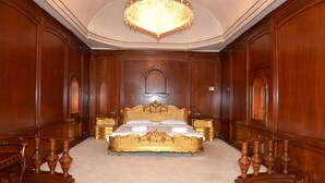 A large, ornate bed with a gold frame in a room with wooden paneling and a chandelier.