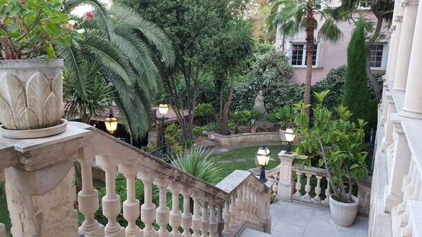 A courtyard with a stone balustrade, potted plants, and a statue.