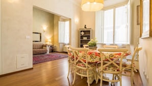 A dining area with a round table, floral tablecloth, and white chairs. There is a chandelier above the table. - Tornaquinci Luxury Penthouse (Firenze)