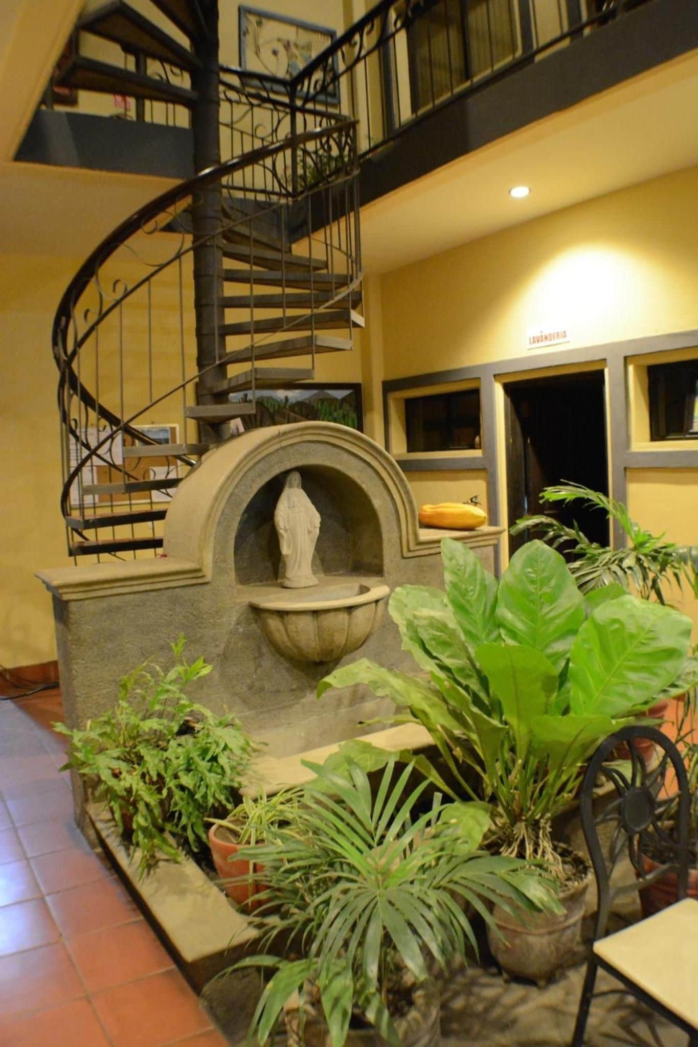 Una escalera en espiral, una fuente y plantas en macetas en un vestíbulo.