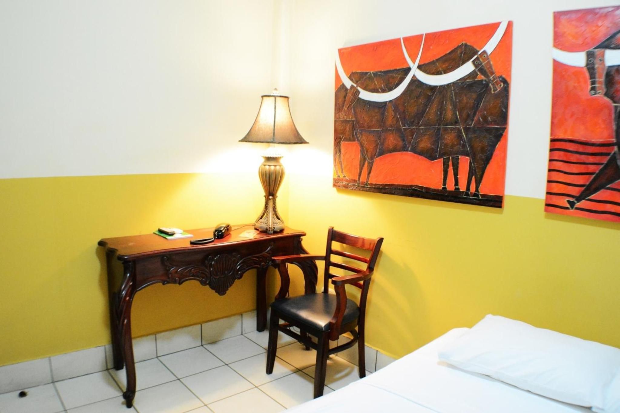 A room with a desk, chair, lamp, and paintings on the wall.