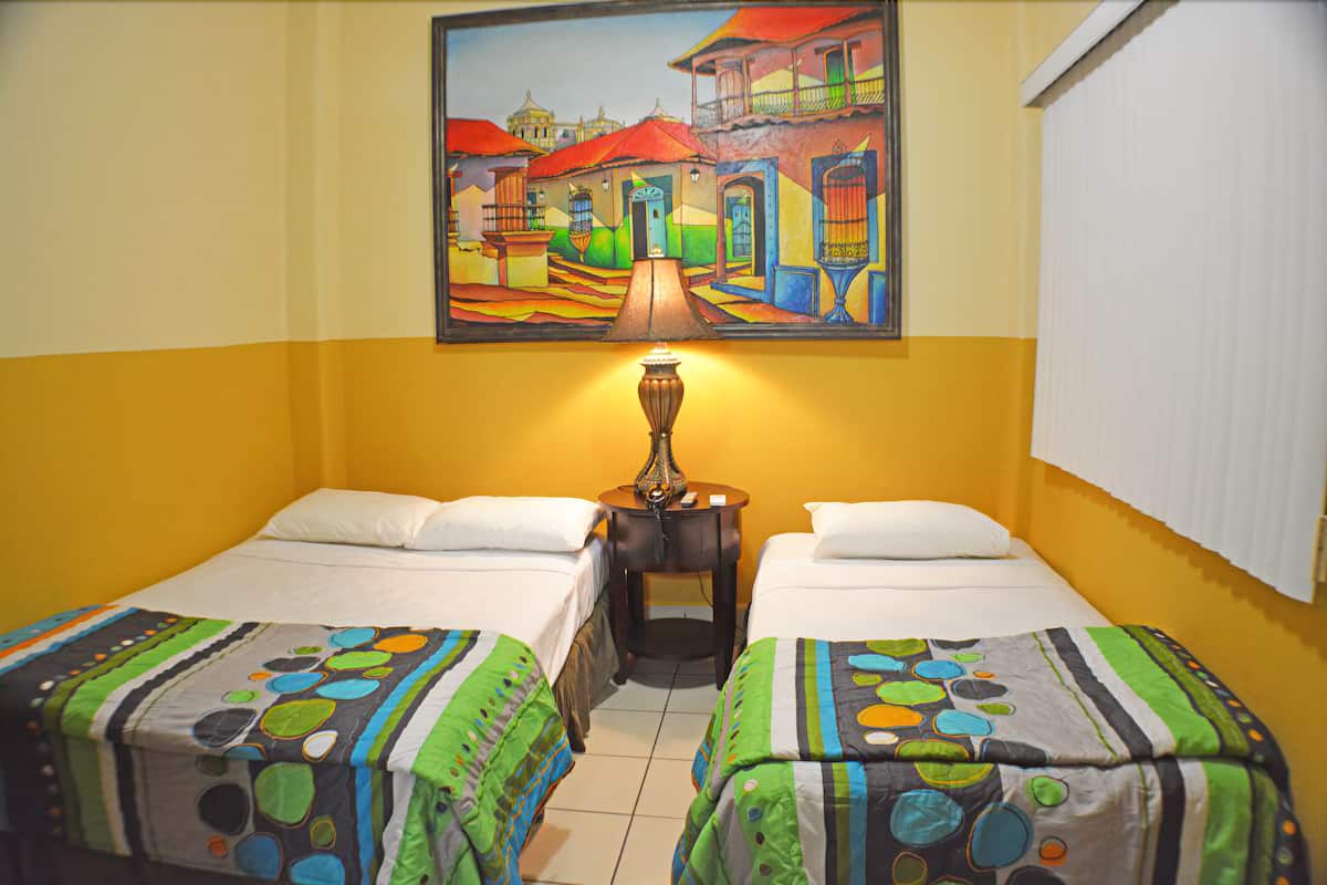 A hotel room with two beds, a painting on the wall, and a lamp between them.