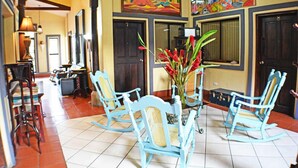 A dining area with a table and four blue rocking chairs, a vase with red flowers, and a painting above the door. - Hotel Los Balcones De Chinandega (Chinandega)