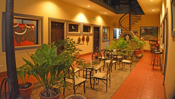 A spacious indoor area with a glass table surrounded by chairs, potted plants, and framed artwork on the walls. - Hotel Los Balcones De Chinandega (Chinandega)