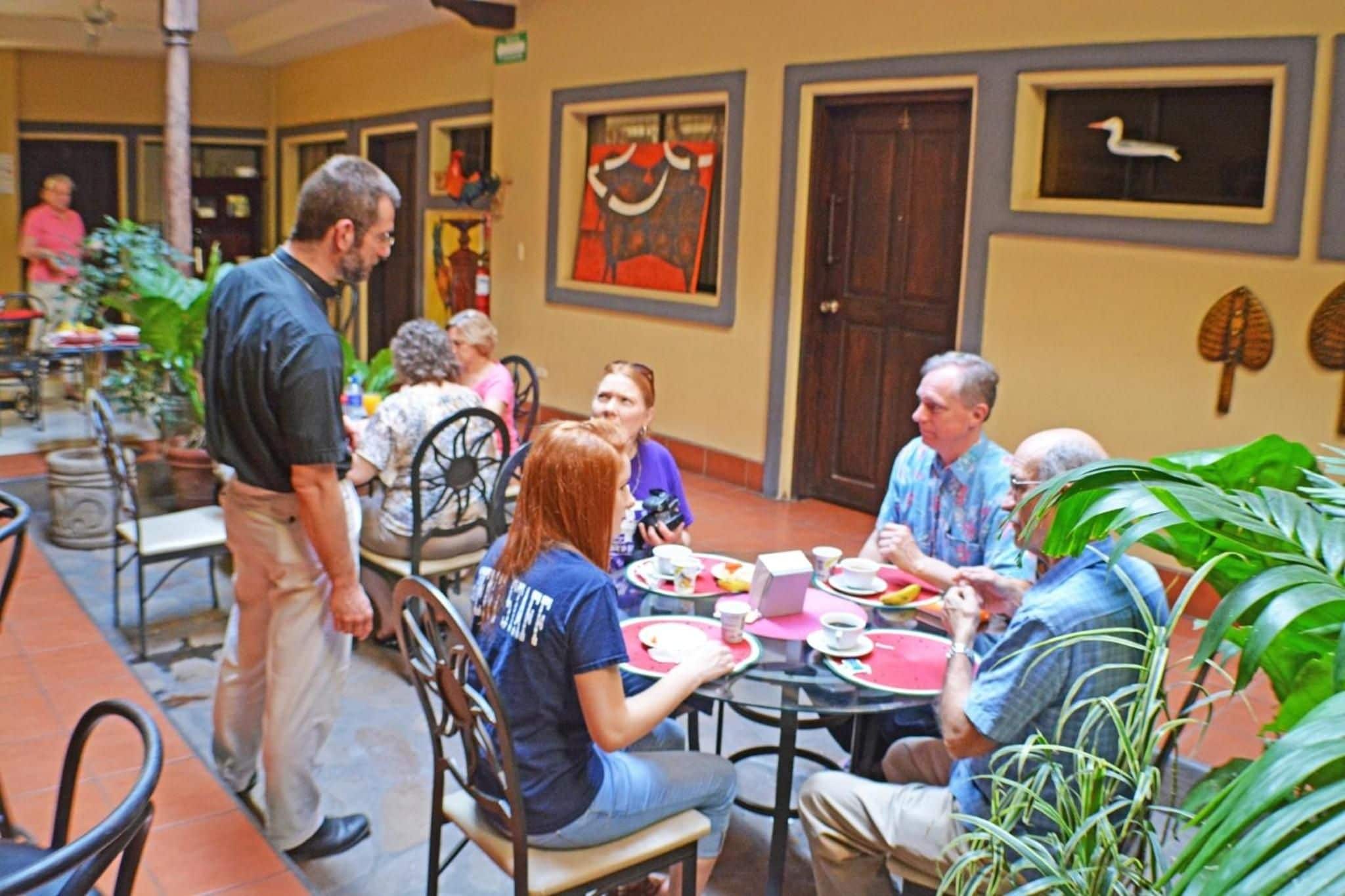 Um grupo de pessoas sentadas em mesas redondas em um café, com cadeiras e mesas dispostas em círculo.
