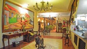 A lobby with a large mural, a chandelier, a reception desk, and a staircase. - Hotel Los Balcones De Chinandega (Chinandega)