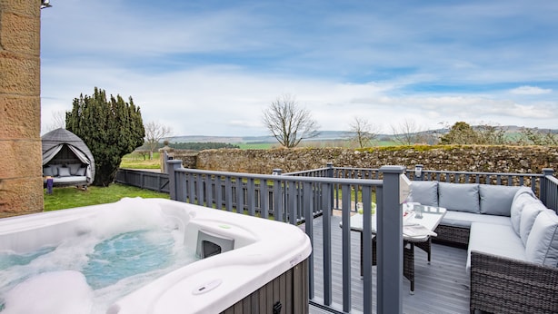 A hot tub on a deck with outdoor furniture, a stone wall, and a view of the countryside. - Hot tub, spa-like garden, log burner (Chatton)