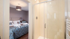 A modern bedroom with a large bed, a glass-enclosed walk-in closet, and a shower area. - Hot tub, spa-like garden, log burner (Chatton)
