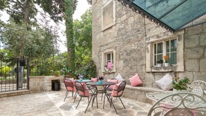 A stone patio with a round table and chairs, a stone wall, and a window with a plant. - Authentic Stone Villa In The Heart Of Split, Next To Diocletian's Palace  (Split)