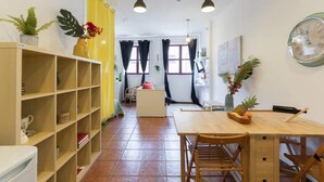 Una stanza accogliente e ben illuminata, con un tavolo da pranzo in legno, sedie e una libreria piena di libri e oggetti decorativi.