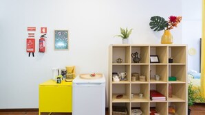 Una stanza con una scrivania gialla, un elettrodomestico bianco, una libreria in legno e una piccola pianta.