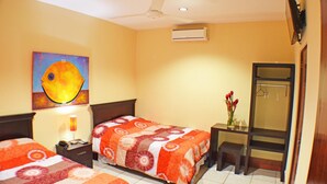 Ein Hotelzimmer mit zwei Betten, einem Deckenventilator, einer Klimaanlage, einem kleinen Tisch mit Blumenvase und einem Spiegel.