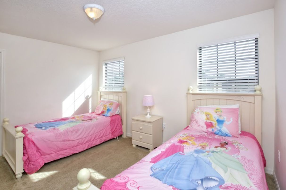 Ein Schlafzimmer mit zwei Einzelbetten, jeweils mit einer rosa Tagesdecke und passenden Kissen, einem Nachttisch mit Lampe und einem Fenster mit Jalousien.