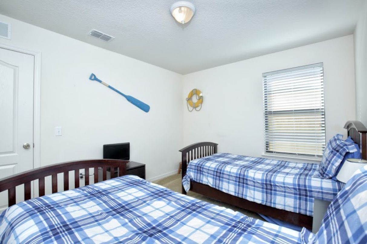 Une chambre avec deux lits, un bureau, une chaise, une télévision et une fenêtre avec des stores.