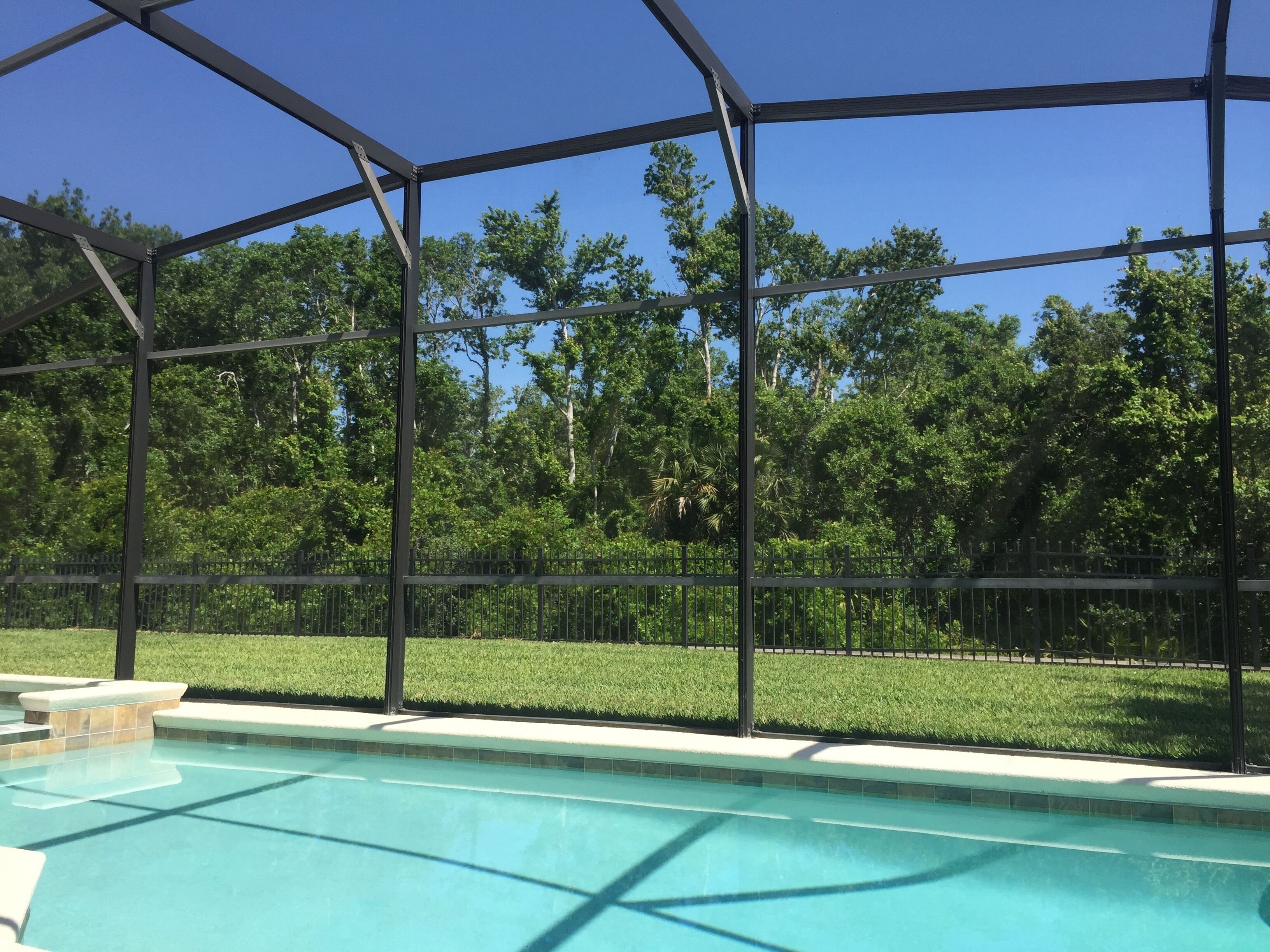 Piscina con una cerca metálica y vistas a árboles y césped.