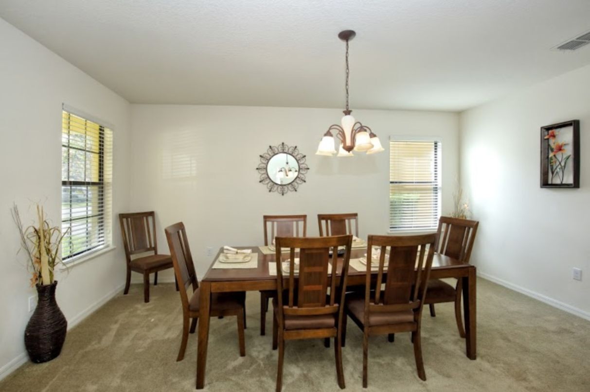 A dining room with a wooden table and chairs, a chandelier, and a vase with dried plants.