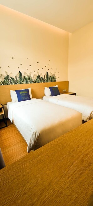 Habitació d'hotel amb dos llits, ambres de fusta i un mur decorat amb un dibuix de fulles tropicals.