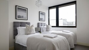 A hotel room with two beds, a large window, and artwork on the walls.