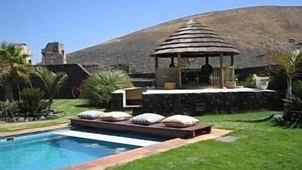 A pool with a stone border, a gazebo, and a stone wall.