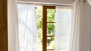A bedroom with a bed, a window with curtains, and a view of greenery outside.
