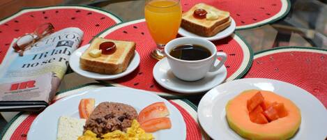 A breakfast setting with toast, scrambled eggs, rice, and a melon slice on a table with a newspaper and a glass of orange juice.