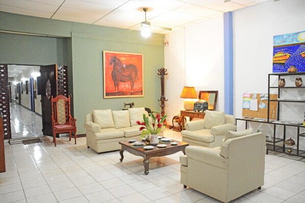 A hotel lobby with a sofa set, a coffee table with flowers, a guitar, and a painting on the wall. - Hostal del Pacifico (Chinandega)