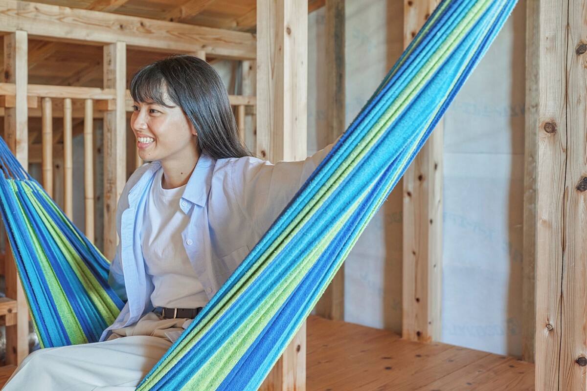 A person sitting in a hammock inside a wooden cabin with a wooden floor and walls.