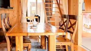 A wooden dining table with chairs, a television on a shelf, and a bookshelf. - Pension Snadun (Ginoza)