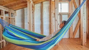 A hammock suspended between wooden beams in a room with exposed wooden walls and a sloped ceiling. - Pension Snadun (Ginoza)