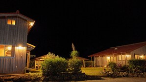 A rustic wooden building with a red-tiled roof, a small porch, and a well-lit entrance. - Pension Snadun (Ginoza)