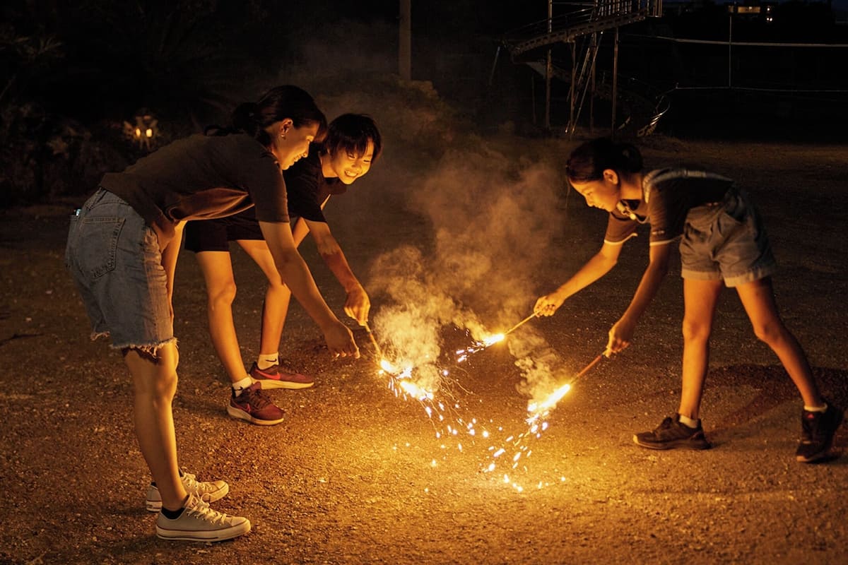 Three people lighting sparklers on a road at night.