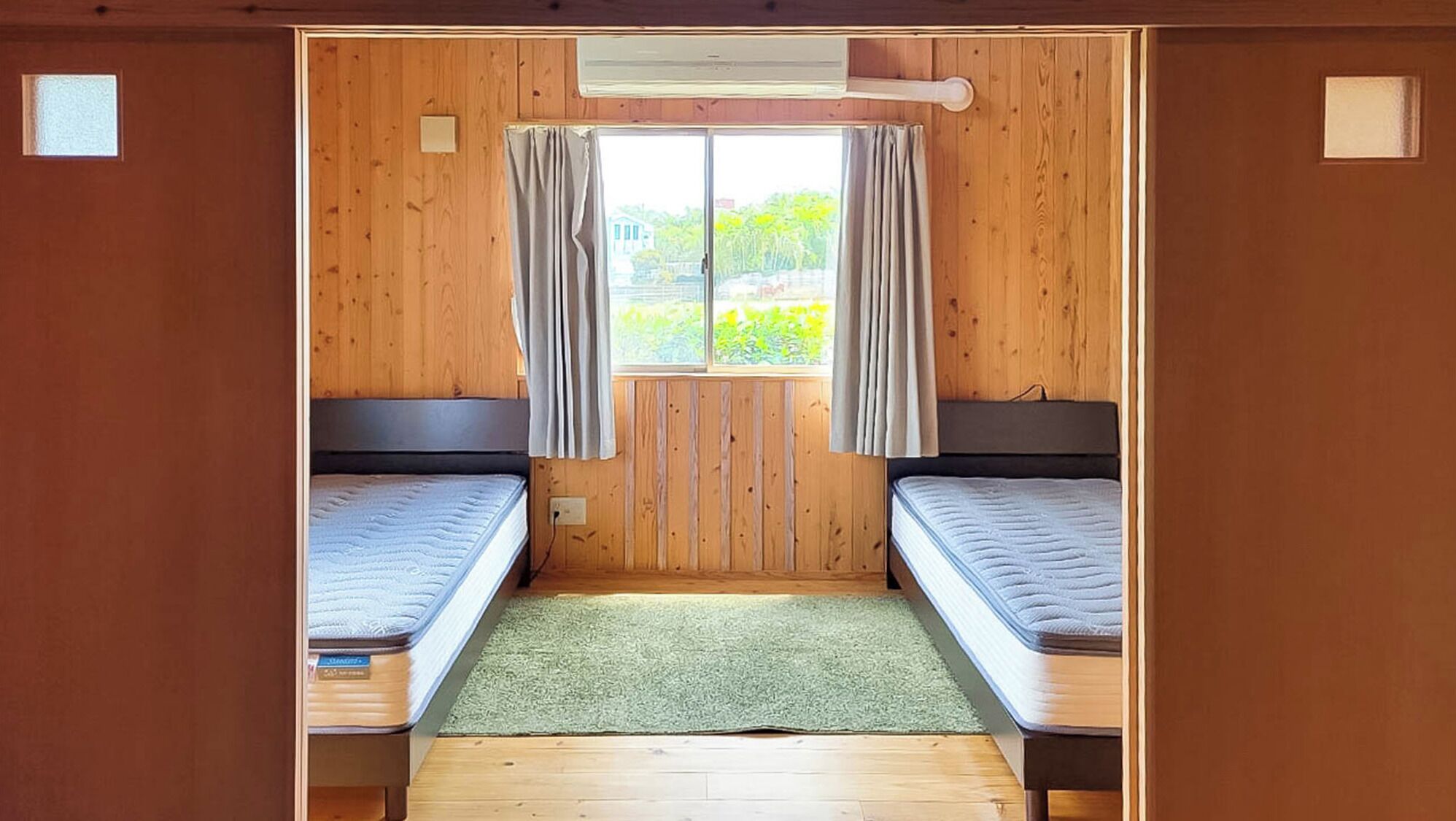 A room with two beds, a window with curtains, and a green mat.