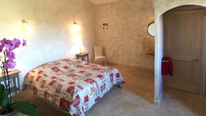 Een slaapkamer met een bed, een stoel, een klein tafeltje, een spiegel en een deur.