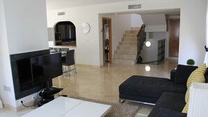 A modern living room with a flat-screen TV, a white coffee table, a dark sofa, and a staircase leading to an upper floor. - Beautiful Detached Spacious Villa, Amazing views, Private Heated Pool, WiFi, A/C (La Manga Club)