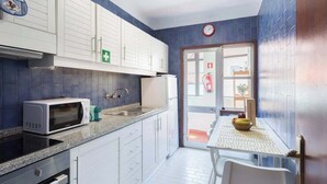 A kitchen with white cabinets, a microwave, a sink, and a table with chairs. - Downtown Lovely Flat by HostWise (Porto)