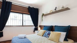 A hotel room with a bed, curtains, a nightstand, a shelf with decorative items, and a window. - Downtown Lovely Flat by HostWise (Porto)
