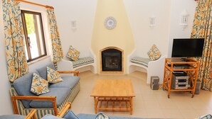 Ein Wohnzimmer mit einer Couch, Sesseln, einem Holztisch, einem Kamin, einem Fernseher und einer Stereoanlage.