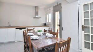 Een moderne keuken met witte kasten, een houten eettafel gedekt voor vier personen en een groot raam.