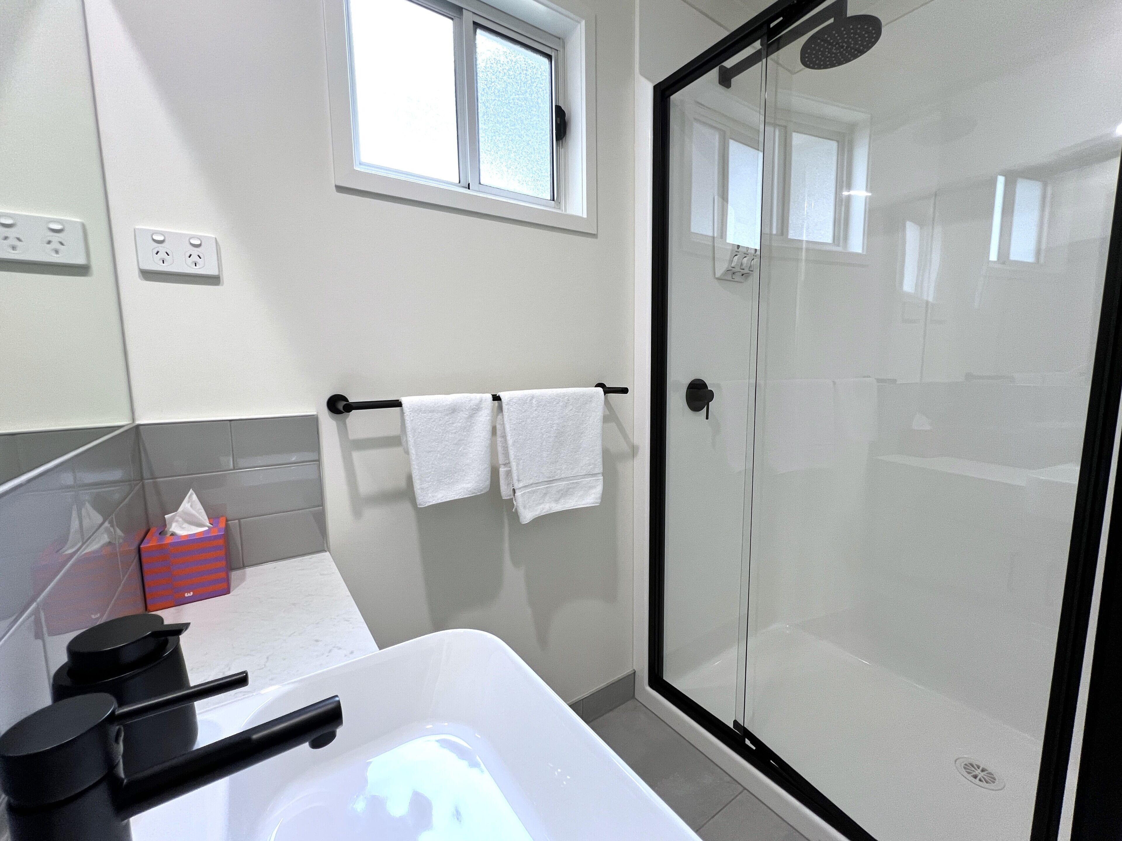 Un baño moderno con ducha acristalada, una bañera blanca y un perchero con dos toallas blancas.