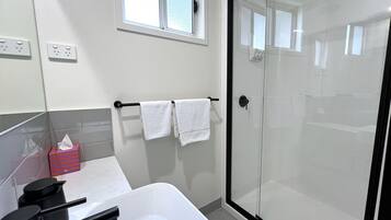 Un baño moderno con ducha acristalada, una bañera blanca y un perchero con dos toallas blancas.
