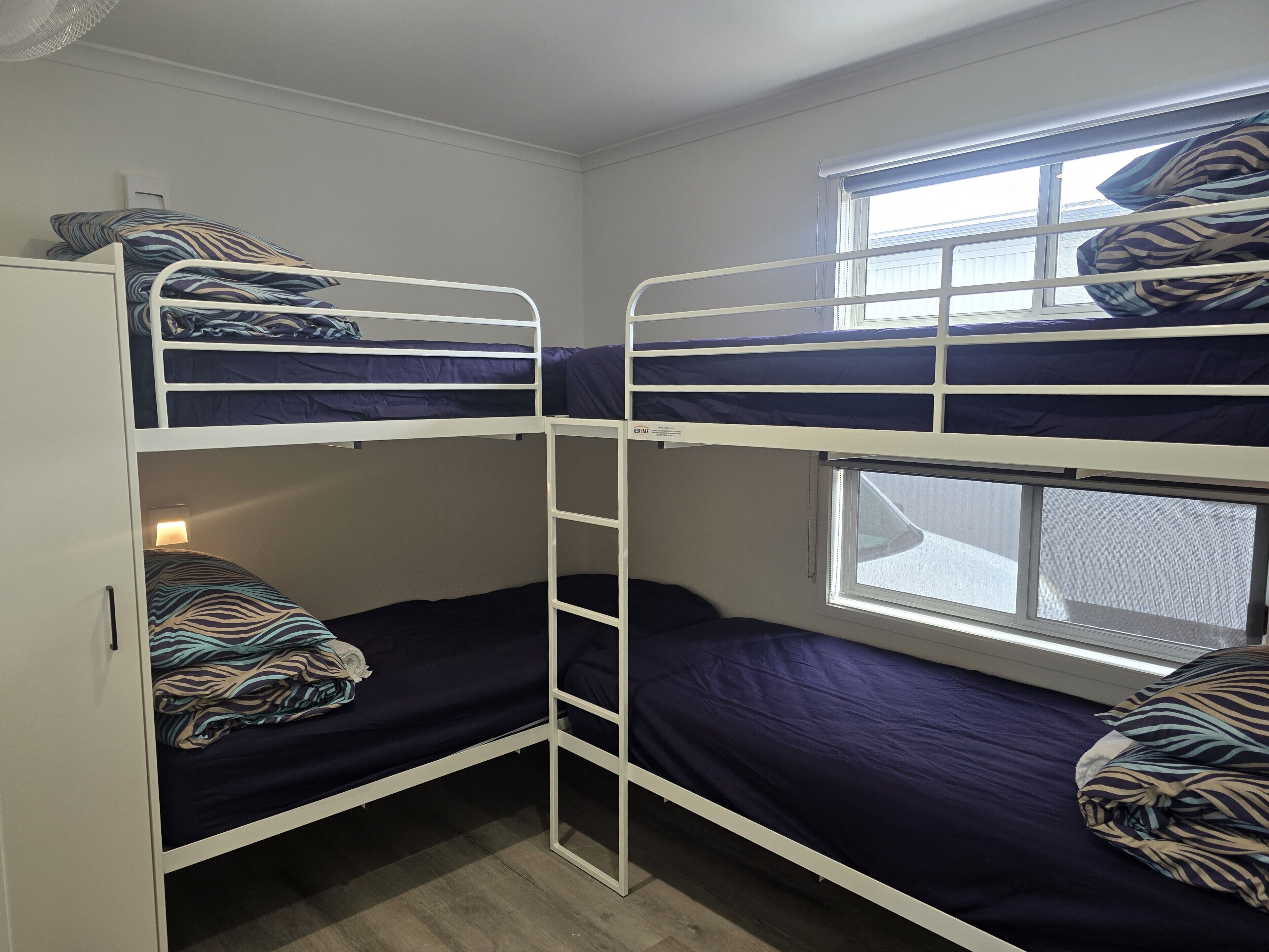 A bunk bed room with a window, a ladder, and a wardrobe.