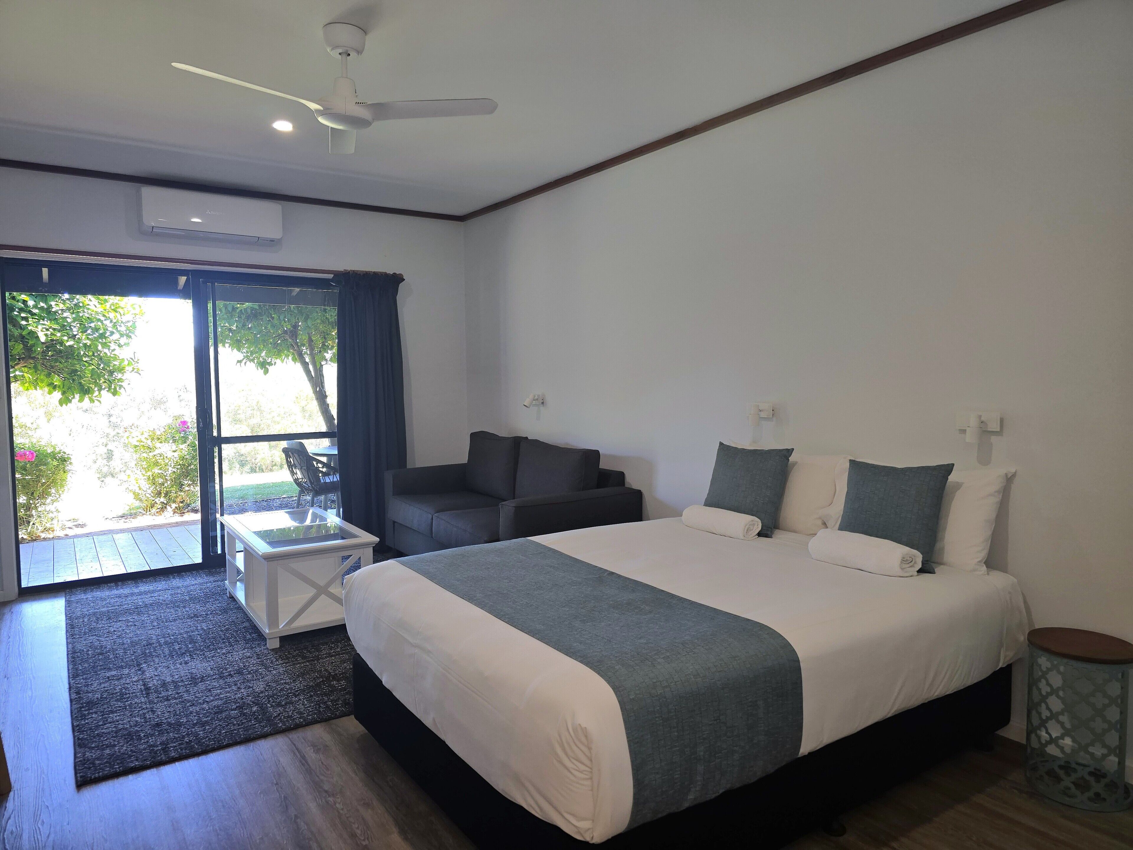 A modern bedroom with a large bed, a sofa, a small table, and a ceiling fan.