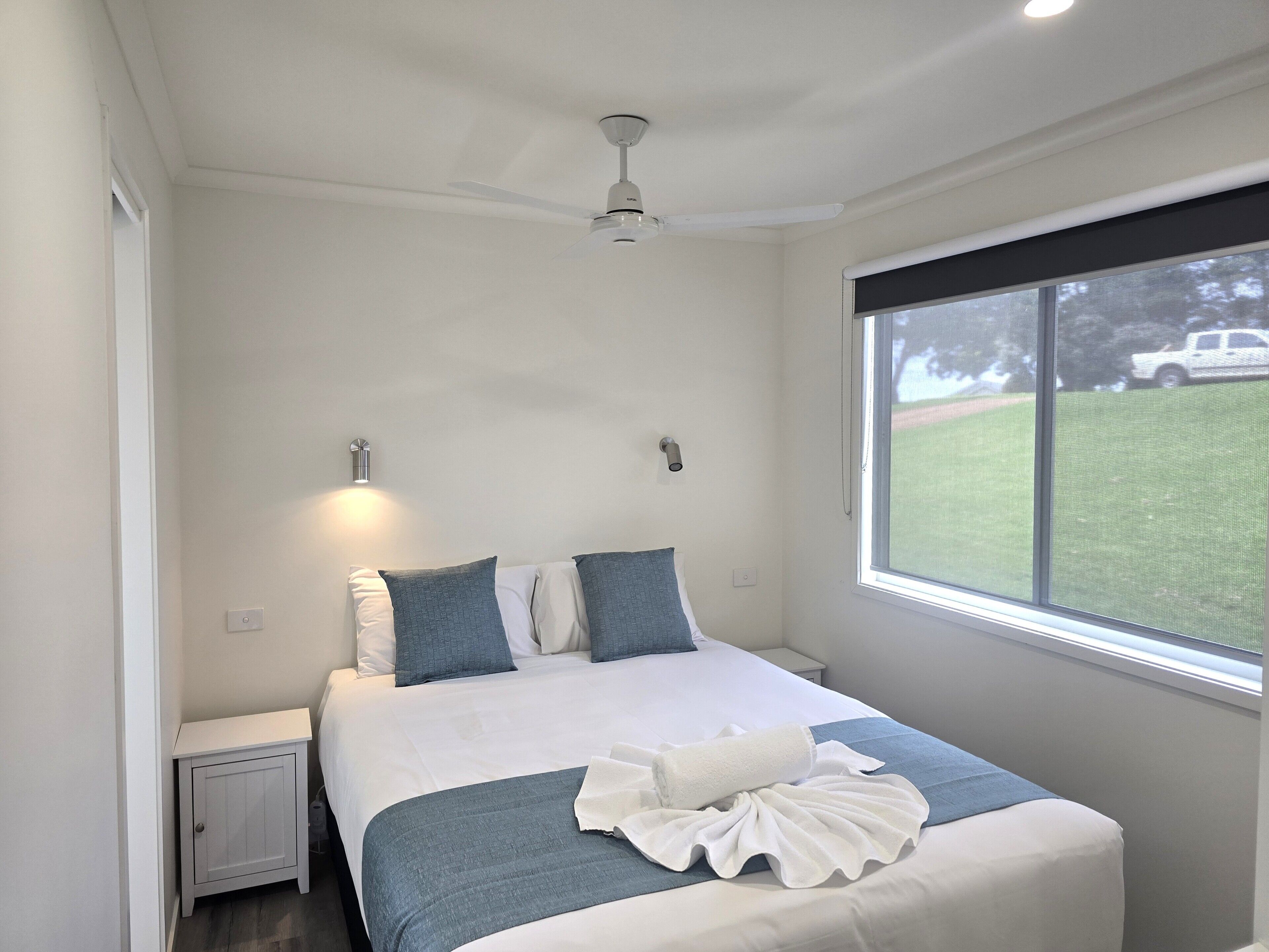A neatly made bed with a white and blue bedspread, two pillows, a white towel, and a ceiling fan.