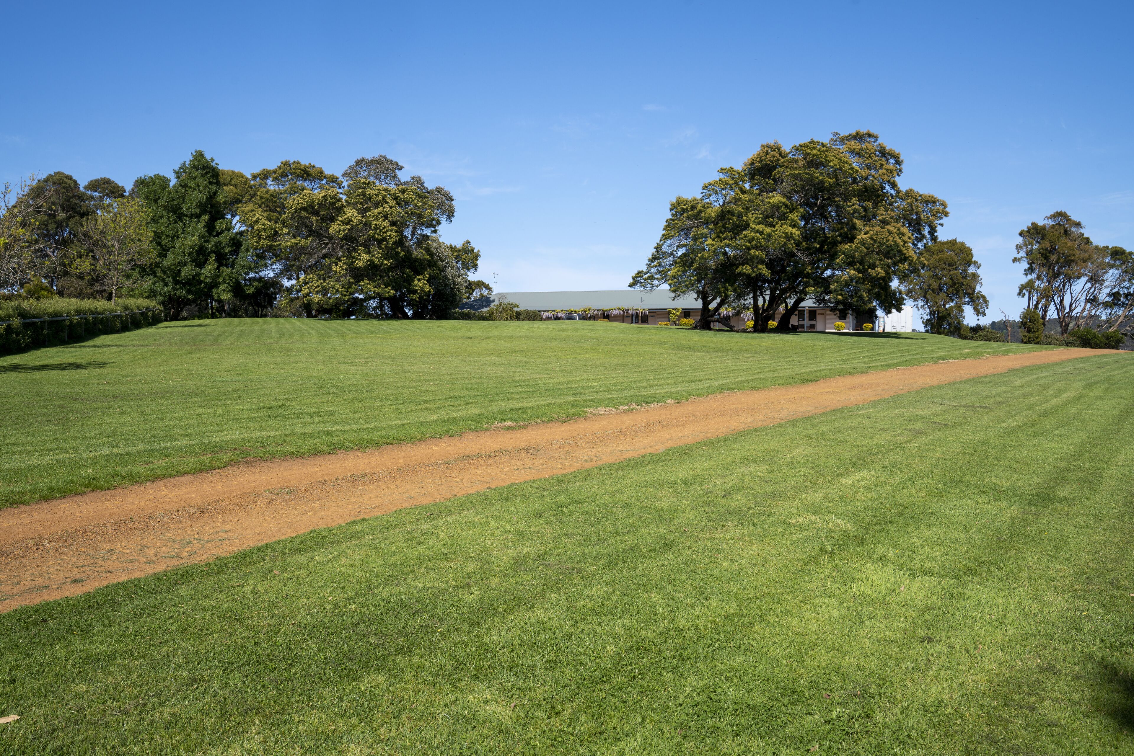 Ein gepflegtes, grünes Feld mit einem Feldweg, umgeben von Bäumen und einem Gebäude im Hintergrund.