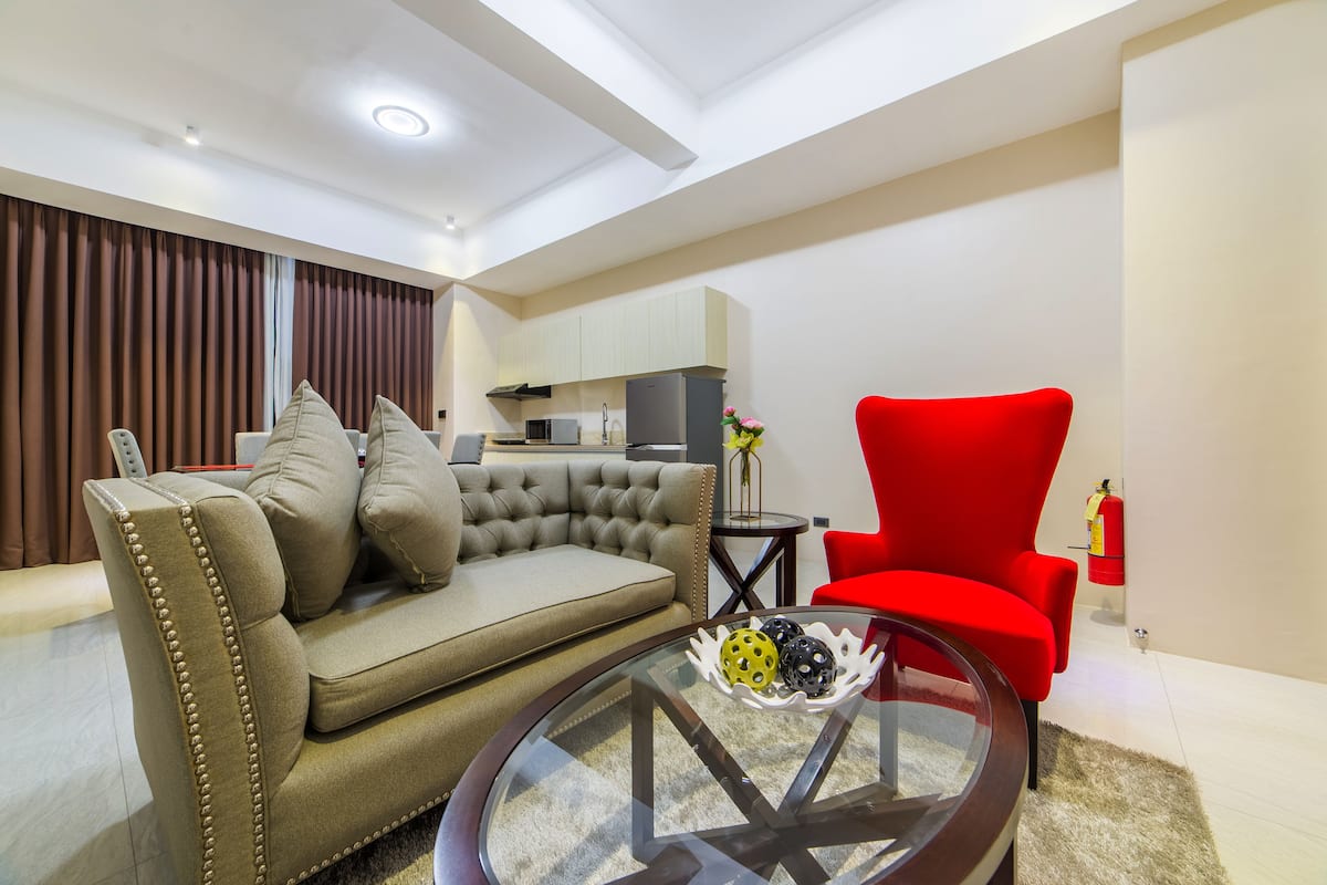 A modern living room with a beige sofa, a red armchair, and a glass coffee table.