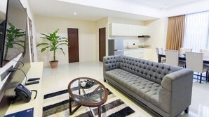 A modern living room with a grey sofa, a TV, a small round table, and a potted plant.