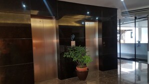 A modern lobby with a marble floor, a potted plant, and two elevators.